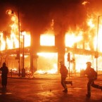 Fire fighters and riot police survey the area as fire rages through a building in Tottenham, north London after members of a community where a young man was shot dead by police took to the streets to demand 