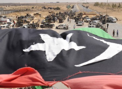 Libyan revolutionary fighters are seen behind the country's new flag while gathering on the main road outside Sirte yesterday.