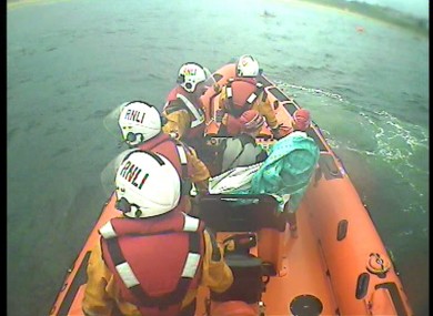 An assisted swimmer wrapped in a green foil blanket is taken ashore.