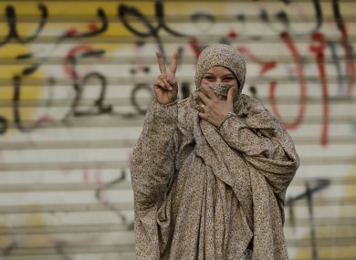 A Bahraini pro-democracy protester gestures in front of a wall sprayed with anti-government graffiti