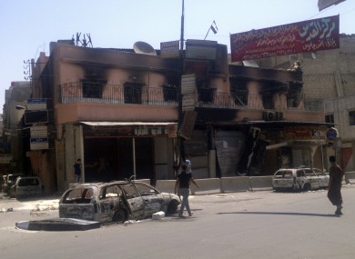 This citizen journalist image shows people walking past a gutted police station flying the Syrian revolutionary flag after fighting between rebels and Syrian troops in the Yarmouk camp for Palestinian refugees in south Damascus, Syria
