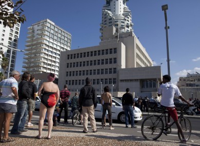 Israelis stand near the scene where a man attacked a security guard at the U.S. embassy, seen in background, in Tel Aviv, Israel