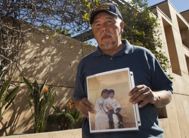 Frank Zamora, 67, holds an old photo of his son Dominic Zamora, then 8, sitting on the lap of his abuser, priest Michael Stephen Baker.