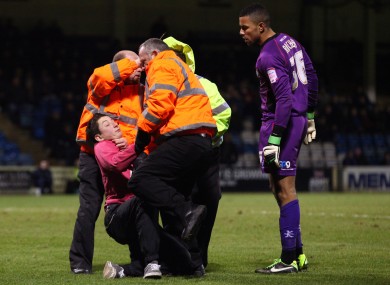 The fan is tackled by stewards as Wycombe goalkeeper Jordan Archer watches on.